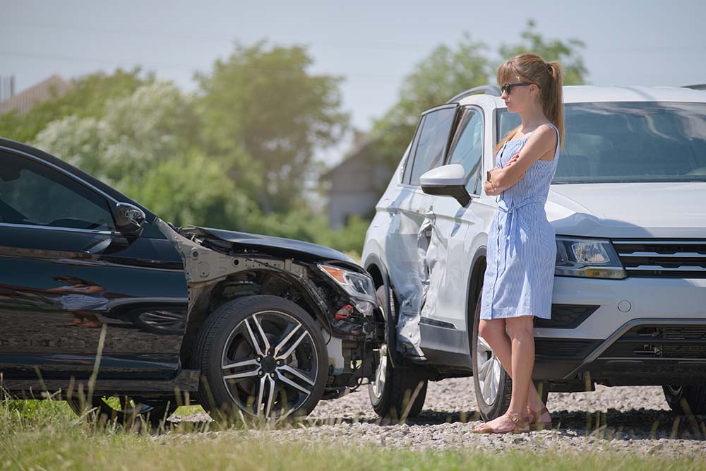 A woman standing next to two wrecked cars