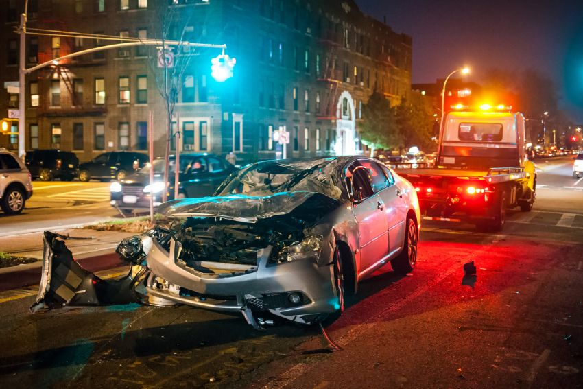 Car crash at night silver car being towed away after front collision debris broken windshield