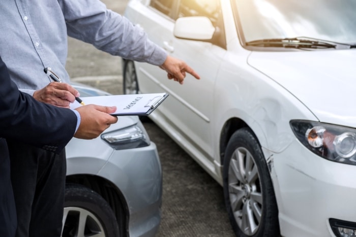 Two men pointing to damage on car with car accident report in hand
